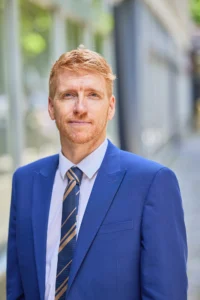 A man in a blue suit and tie standing outside a building.
