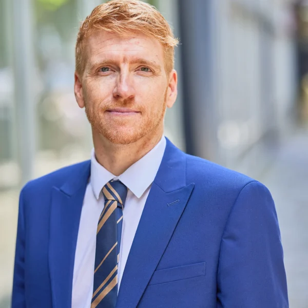A man in a blue suit and tie standing outside a building.