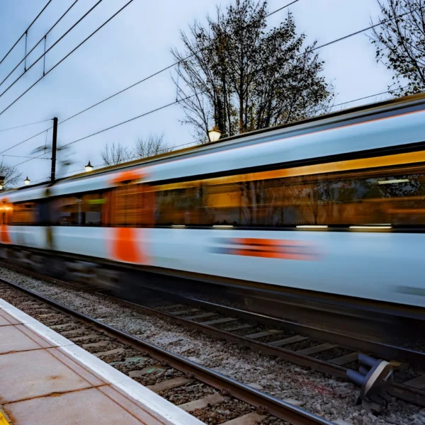A speeding train on a railway track, passing by a platform.