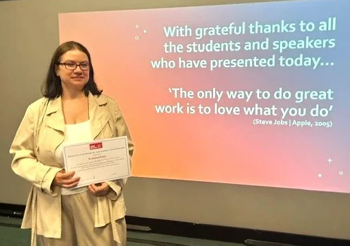 Krystyna stands holding a certificate in front of a presentation slide at the UWE Bristol conference with a thank-you message and an inspirational quote by Steve Jobs.